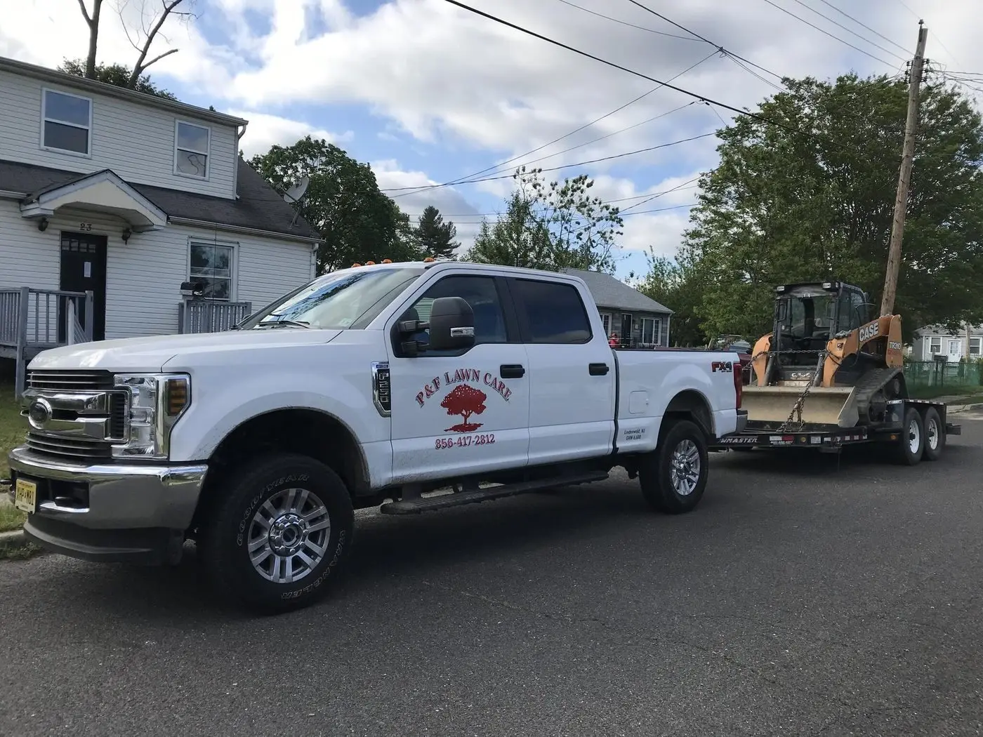 P&F Lawn Care work truck and skid steer on trailer parked on a residential street
