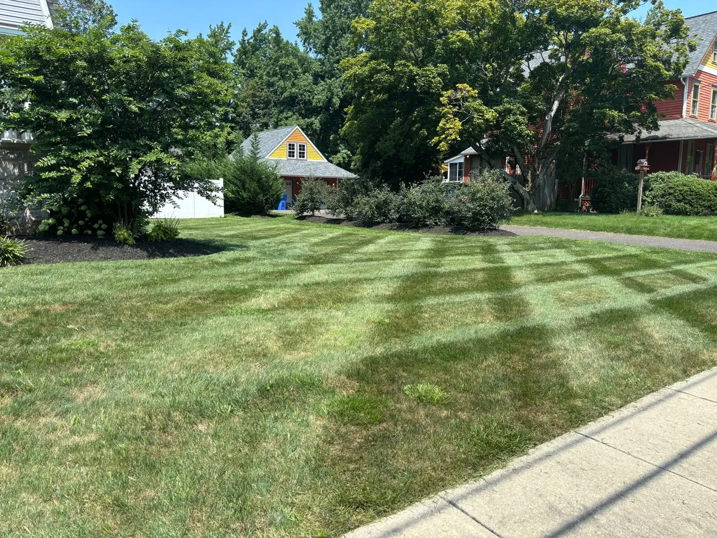 Freshly striped front lawn and mature trees in front of a classic home, maintained by P&F Lawn Care