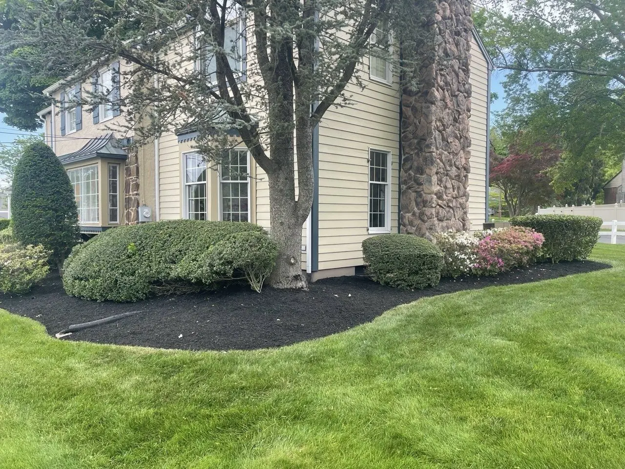 Colonial home with a stone chimney, trimmed shrubs and freshly mulched landscape beds maintained by P&F Lawn Care